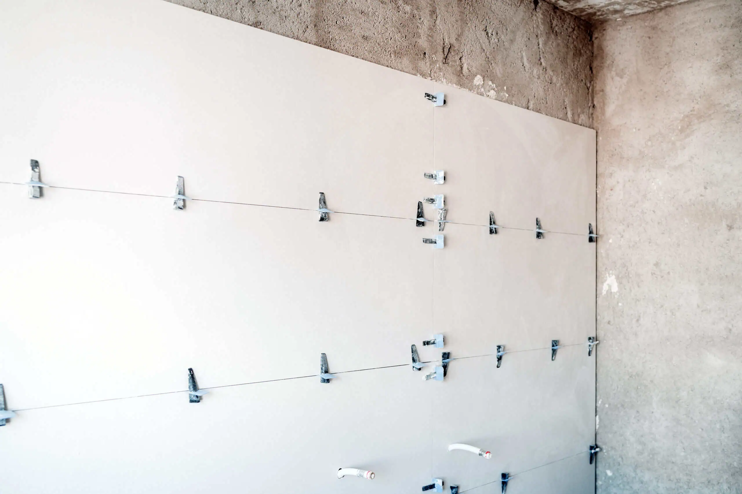 Drywall being installed on a wall with metal fasteners and wires for a smooth finish.