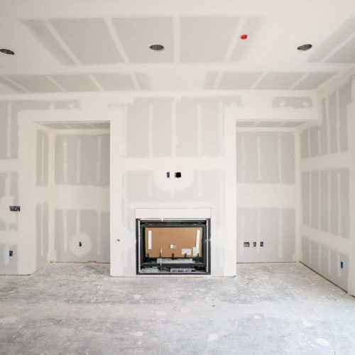 Drywall installation in a modern living room with a fireplace and large sliding glass door.