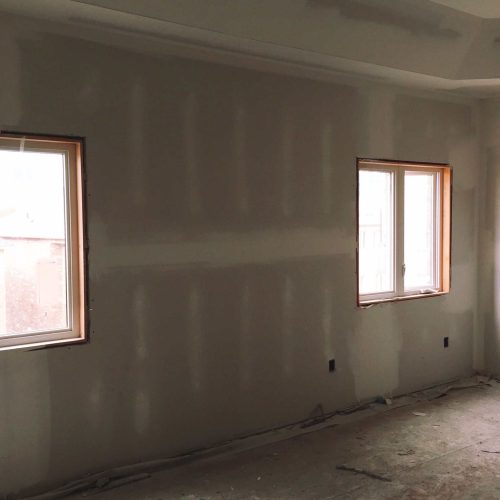Interior drywall installation with unfinished walls and windows in a home renovation.