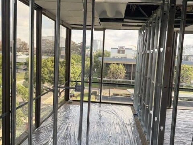 Drywall installation underway in a commercial building with large windows and metal framing.